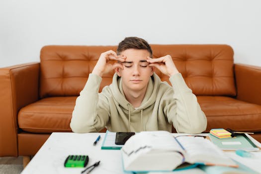 Young man experiencing stress while studying at home, wearing a hoodie.